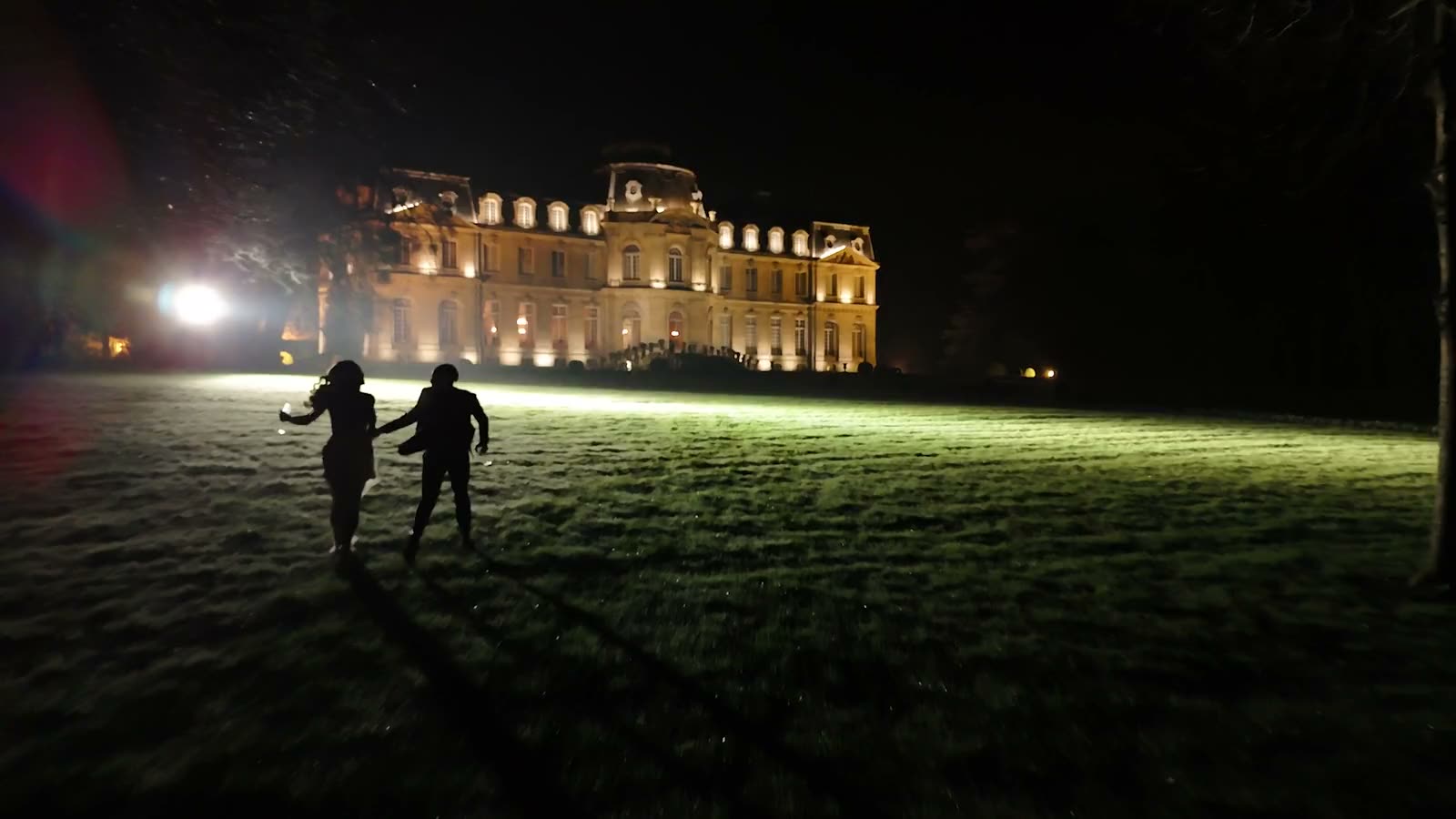 Deux mariés marchent la nuit vers un château illuminé.