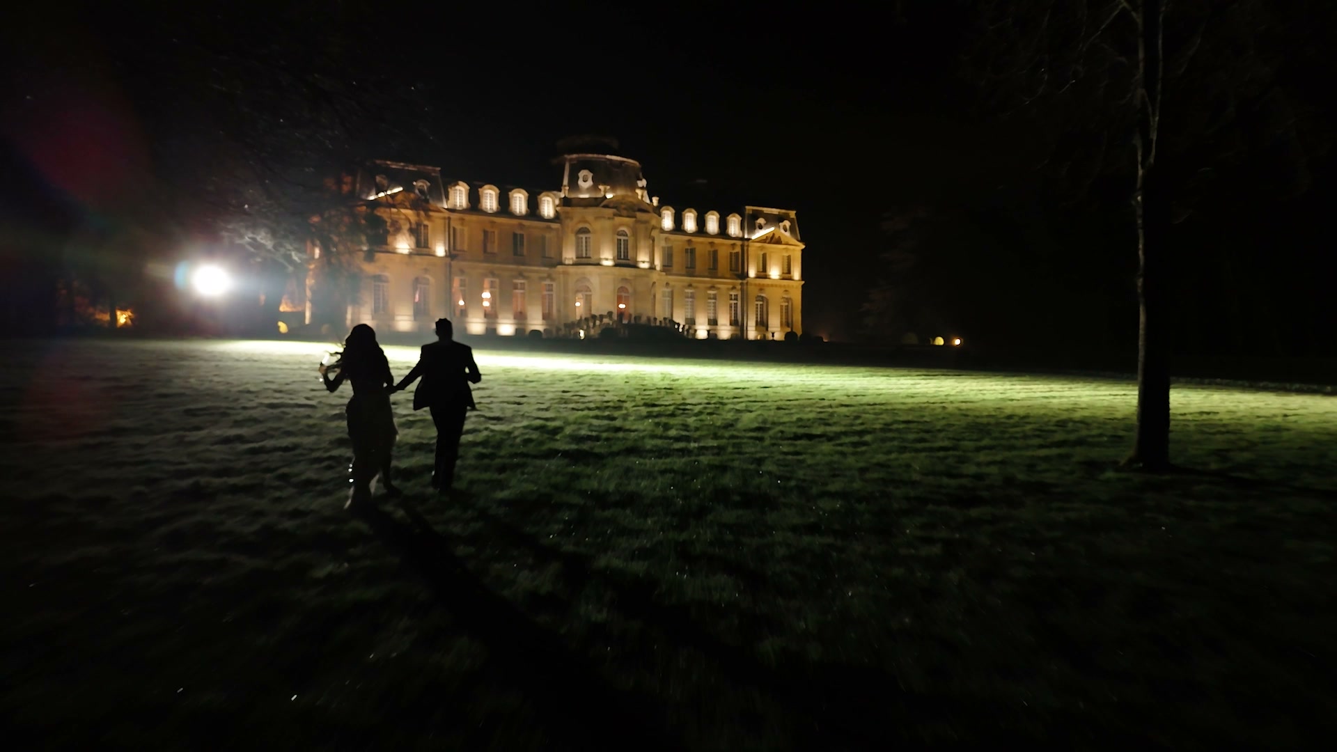 Les mariés marchent la nuit devant le château éclairé.